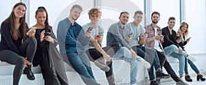 smiling young people with smartphones sitting near an office window.