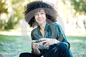 Smiling young photographer enjoying a day in the park sitting on the grass taking photos using her digital camera. Happy