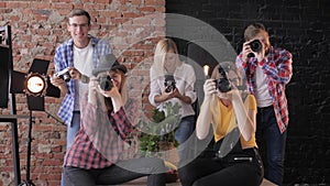 Smiling young photographers with different digital cameras in hands take pictures on background of a brick wall and
