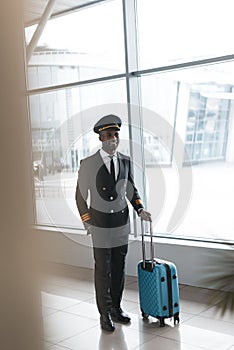 smiling young pilot in professional uniform with suitcase