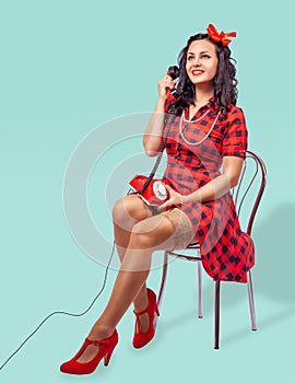 Smiling young pinup woman sitting on a chair and talking on phone