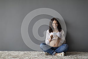 Smiling Young Pregnant Woman Browsing App On Smartphone While Relaxing At Home