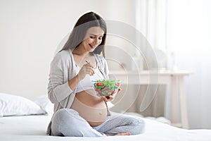 Smiling young pregnant woman eating healthy salad at home
