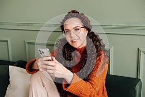 Smiling young pretty woman sitting at home using apps on cell phone technology, happy lady holding smartphone, laughing, looking