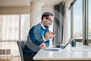 Smiling young professional gesturing while working on laptop at office desk