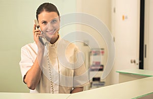 Smiling young receptionist talking on phone at checkout counter