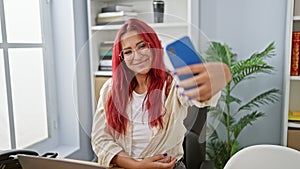 Smiling young redhead business woman taking a selfie at work, capturing her successful day at the office on her smartphone