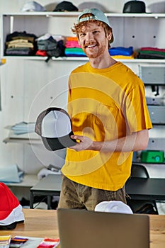 Smiling young redhead designer holding snapback