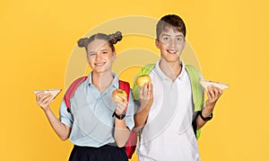 Smiling young schoolchildren with colorful backpacks holding apples and sandwiches