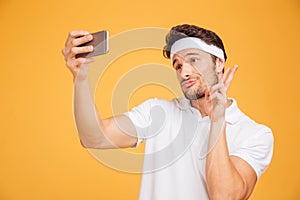 Smiling young sports man taking selfie and showing v sign