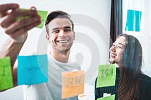 Smiling young startup people have meeting and using glass note sticky wall while creativity work in smart office studio