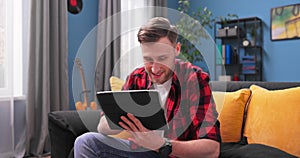 Smiling young student man using digital tablet at home, millennial male user holding computer looking