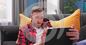 Smiling young student man using digital tablet at home, millennial male user holding computer looking