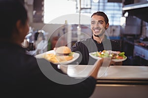 Smiling young waiter giving food to waitress at counter