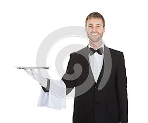 Smiling young waiter holding empty serving tray