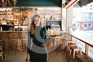 Smiling young waitress standing with a tray of drinks