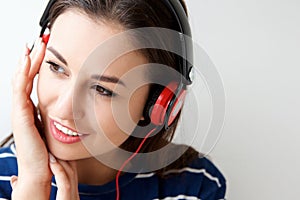 Smiling young woman against white wall listening to music with headphones