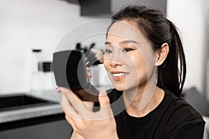 Smiling Young Woman Applying Makeup with Brush Mirror