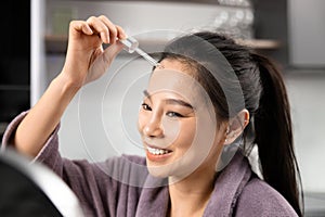 Smiling Young Woman Applying Serum in Front of Mirror