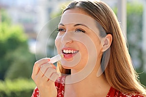 Smiling young woman applying sun protection on her lip outdoor