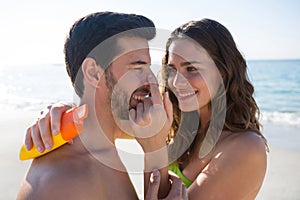 Smiling young woman applying sunscream on man nose at beach