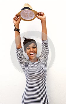 Smiling young woman with arms raised and holding hat