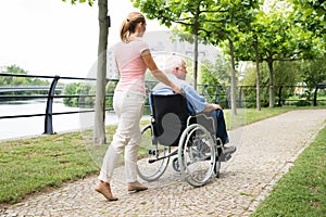 Smiling Young Woman Assisting Her Disabled Father On Wheelchair