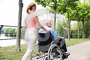 Smiling Young Woman Assisting Her Disabled Father On Wheelchair