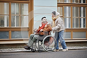 Smiling young woman assisting man in wheelchair in date together in city streets