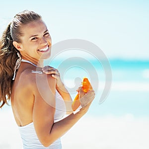 Smiling young woman on beach applying sun block creme