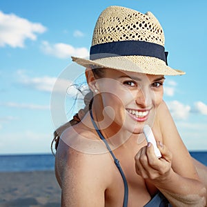 Smiling young woman on beach applying sun protection lipstick