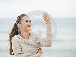 Smiling young woman on beach taking self photo using cell phone