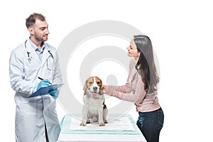 smiling young woman with beagle and veterinarian writing in clipboard