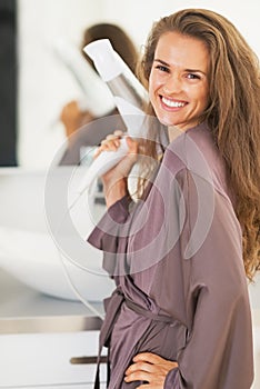 Smiling young woman with blow dryer in bathroom