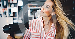 Smiling young woman blow drying hair