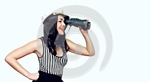 Smiling young woman brunette sailor looks through binoculars, pin-up style on a white