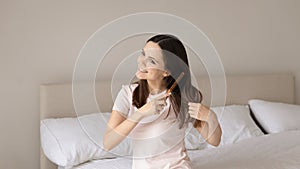 Smiling young woman brush healthy hair in bedroom