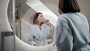 Smiling young woman brushing teeth in bathroom