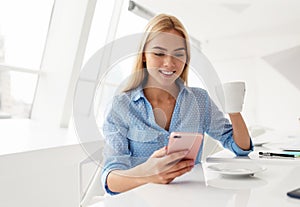 Smiling young woman with cellphone in hand while drinking coffee in a white room photo