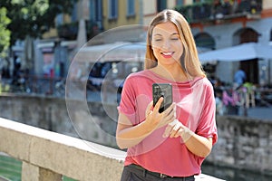 Smiling young woman chatting with mobile phone on Navigli canals in Milan, Italy