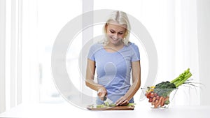 Smiling young woman chopping celery at home
