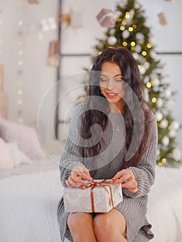 Smiling young woman with christmas present box near christmas tree