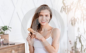 Smiling young woman combing hair at home