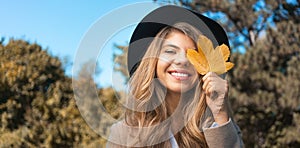 Smiling young woman covering face with a yellow leaf