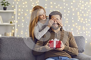 Smiling young woman covering her boyfriend`s eyes and giving him a surprise present