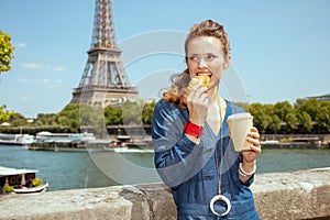 Smiling young woman with cup of coffee eating croissant
