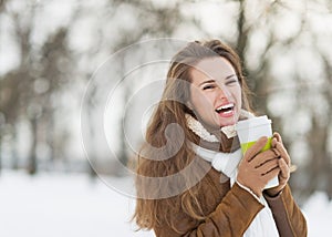 Smiling young woman with cup of hot beverage in winter park