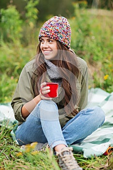 Smiling young woman with cup sitting in camping