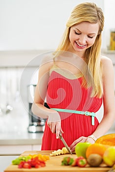 Smiling young woman cutting fresh fruits salad