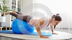 Smiling young woman doing exercises and balancing on fitball at living room. Concept of healthcare, sports and yoga at home